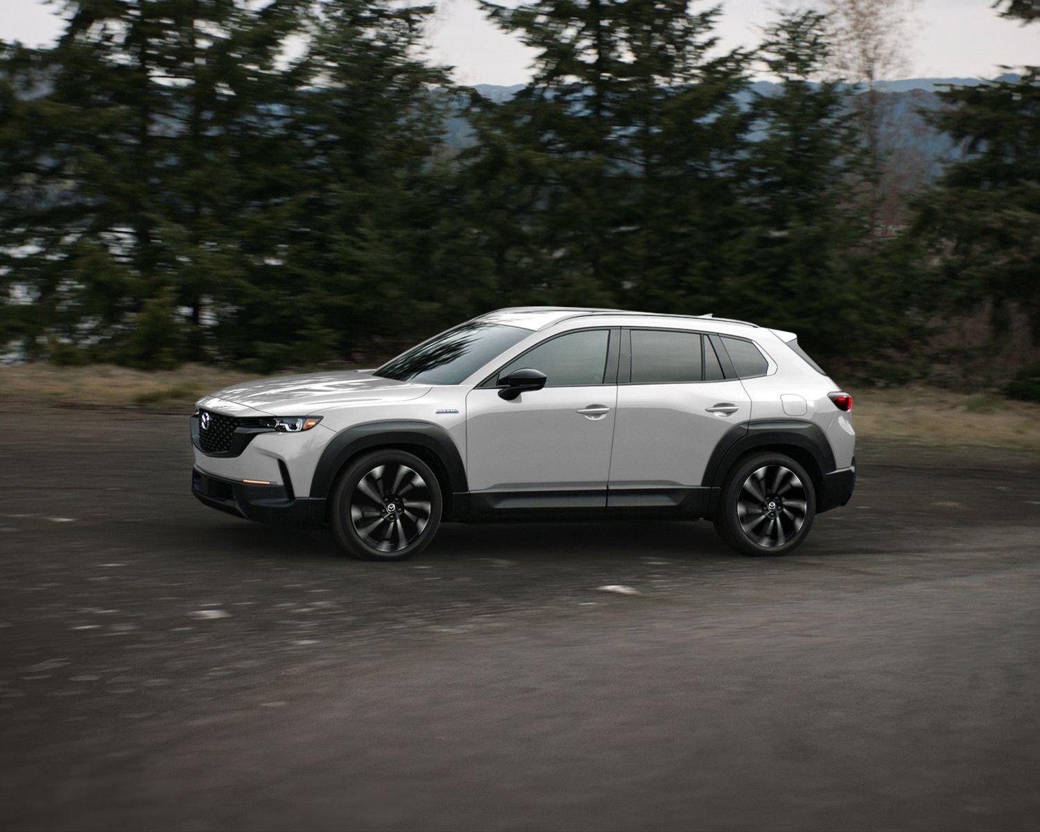 Side profile shot of the 2025 Mazda CX-50 Hybrid driving on dirt road.