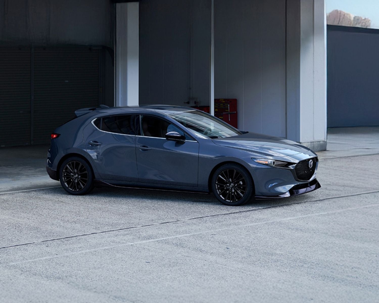 Side profile shot of the 2026 MAZDA3 Hatchback parked in front of building.